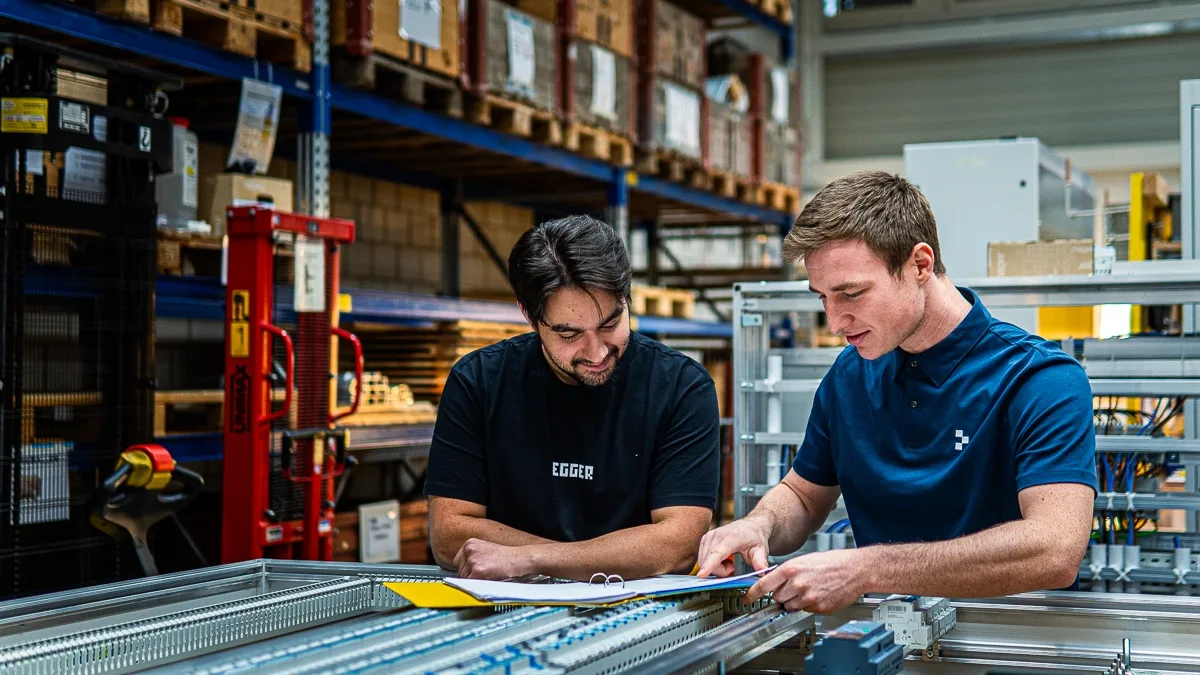 Two workers collaborating over documents in an industrial setting.